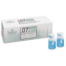 En låda märkt "SILKY 07 SEBO THERAPY TREATMENT 10×10ML" sitter bredvid två små flaskor med blå vätska. Dessa hårprodukter från Silky Sverige riktar sig till fet hårbotten, perfekt för kvinna som söker effektiva hårvårdslösningar.