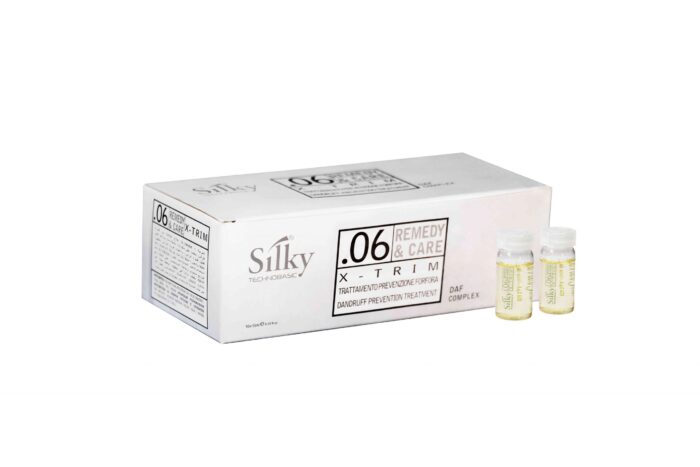 En vit låda märkt "SILKY 06 X-TRIM TREATMENT 10×10ML" sitter bredvid två små genomskinliga flaskor med gul vätska. Detta hårprodukter set är en mjällförebyggande behandling för både män och kvinnor, vilket säkerställer flingfritt hår för alla.